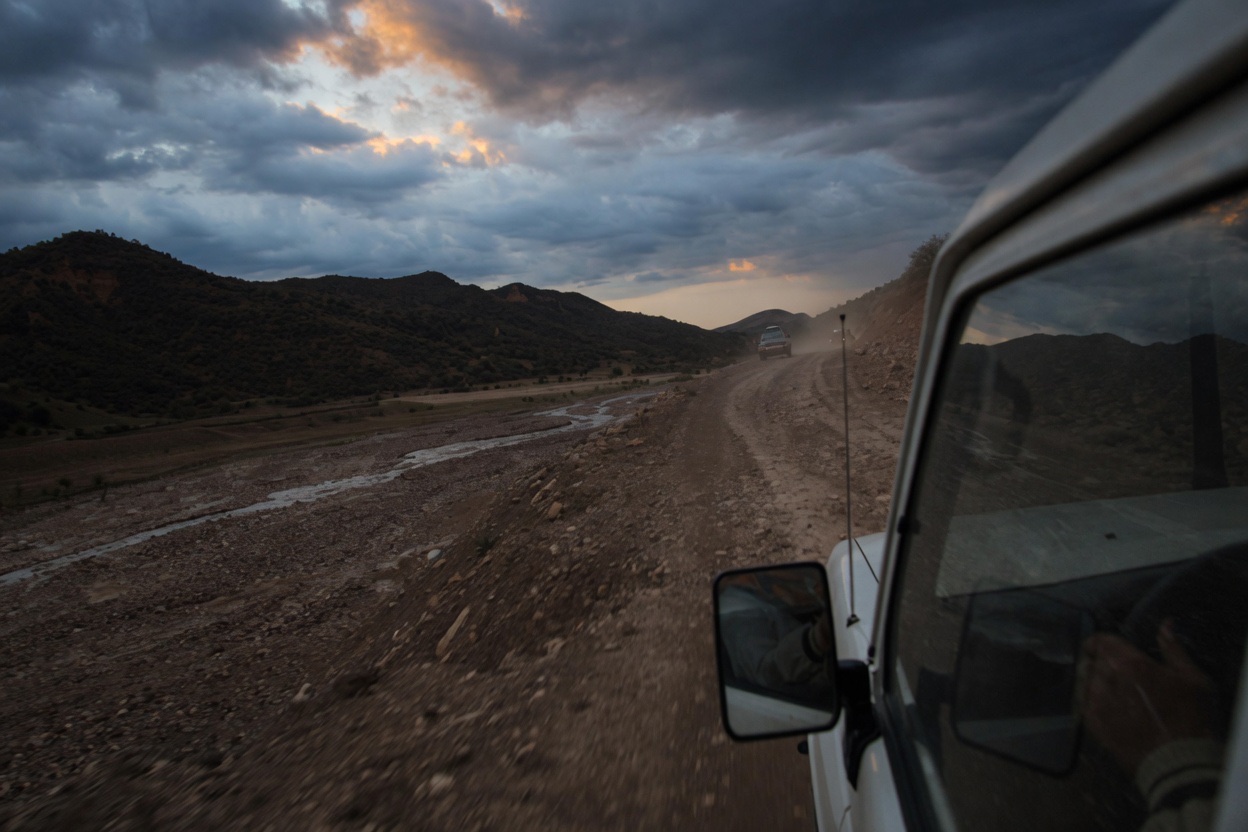 A vehicle on a dirt road beside a dry riverbed, seen from another car